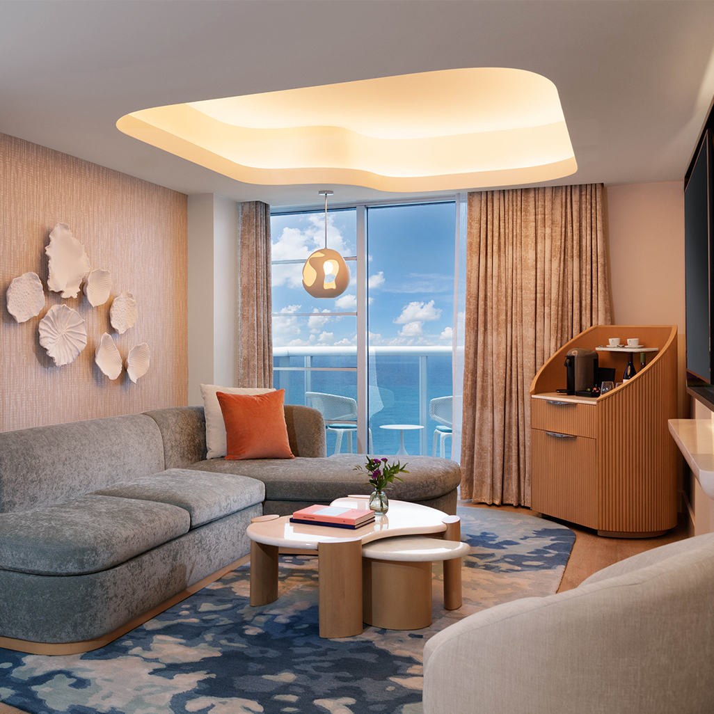 Contemporary ocean-view suite with organic-shaped furniture, a curved sofa, and layered tables in warm natural tones.