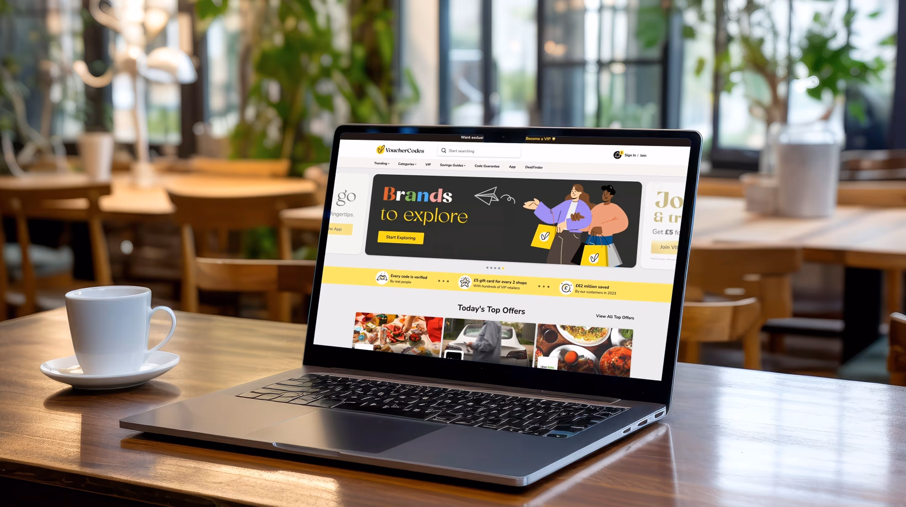 Laptop on a café table displaying the VoucherCodes website with offers and promotions.