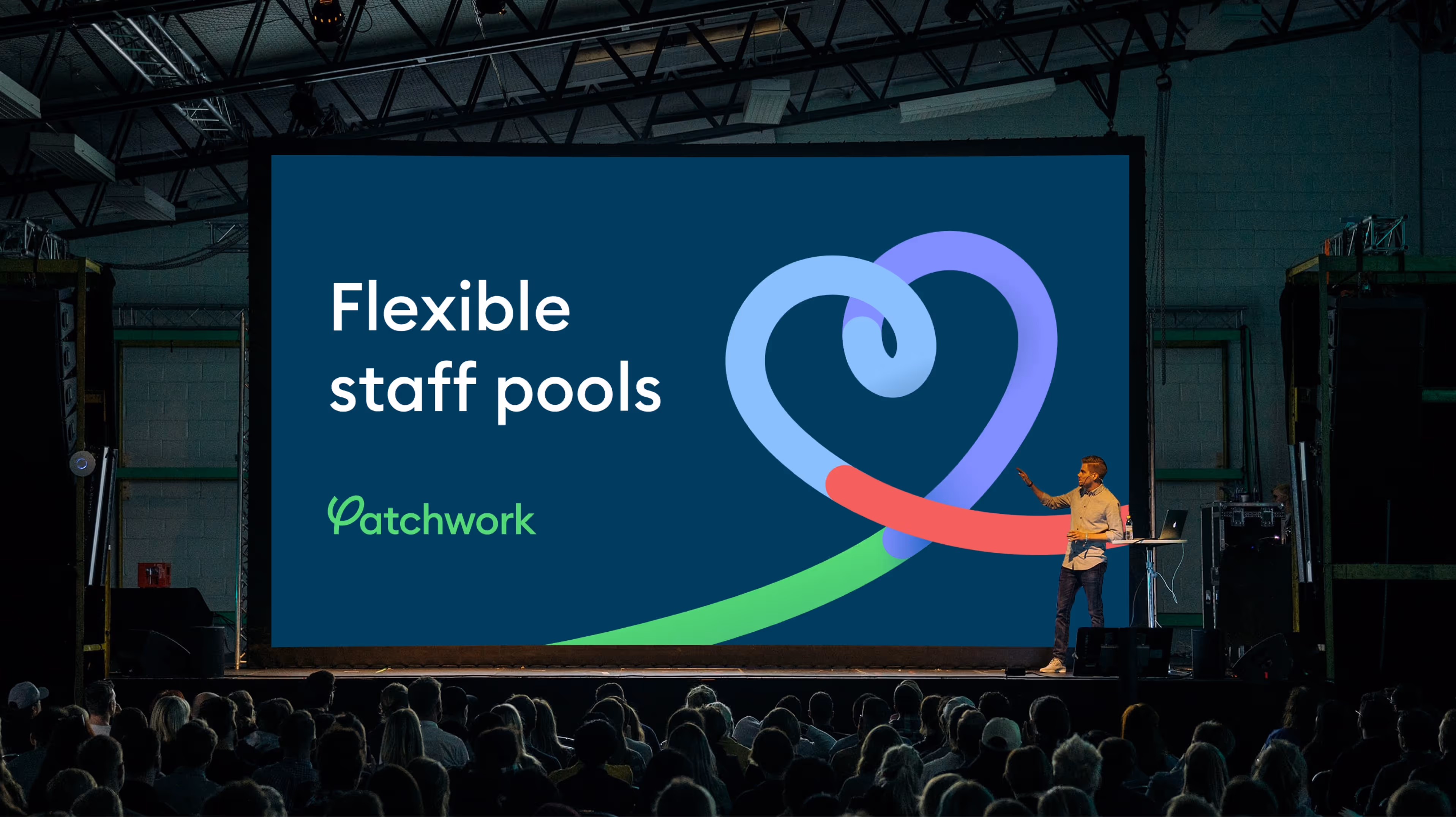 Speaker presenting on stage in front of a large screen showing the Patchwork logo and the words ‘Flexible staff pools.’