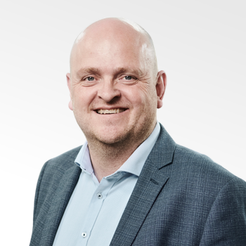 Smiling bald man wearing a blue dress shirt and dark blazer against a light background.