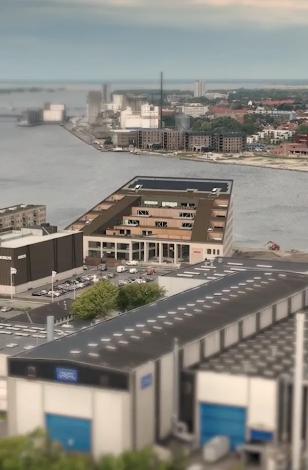 Aerial view of industrial buildings and warehouses near a waterway with a town visible in the background.