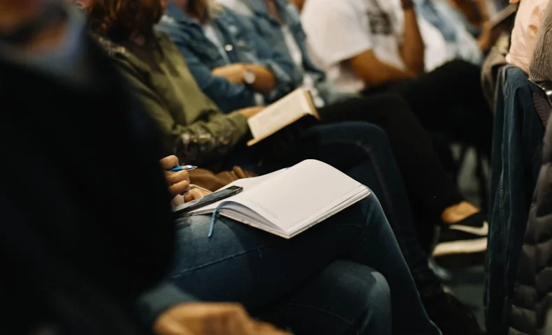Audience members taking notes in notebooks while attending a lecture or class session.