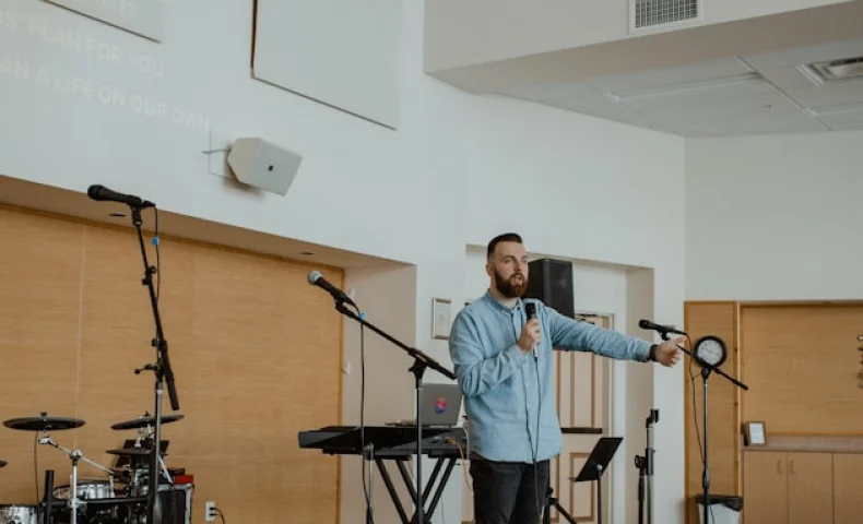 Man speaking on stage with microphone during church presentation.