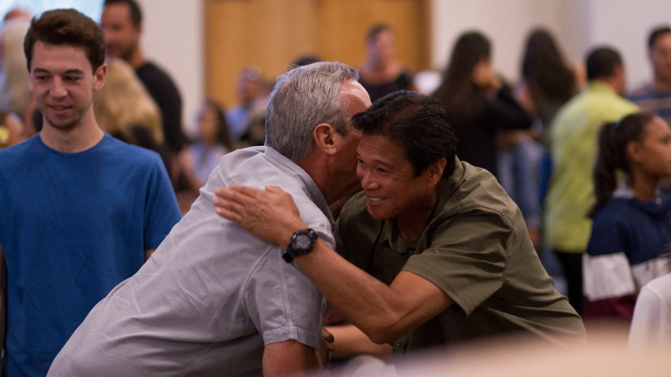 Man smiling and embracing another person during a welcoming moment at church.