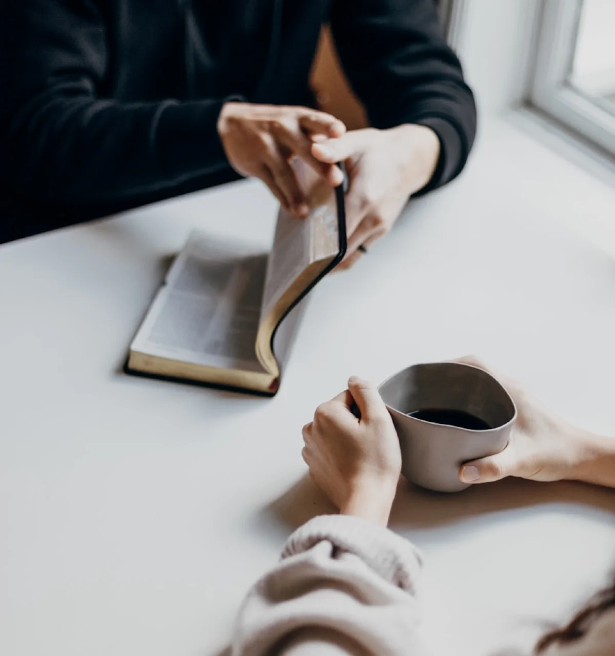 Close-up of hands with a Bible and coffee cup during a personal Bible study.