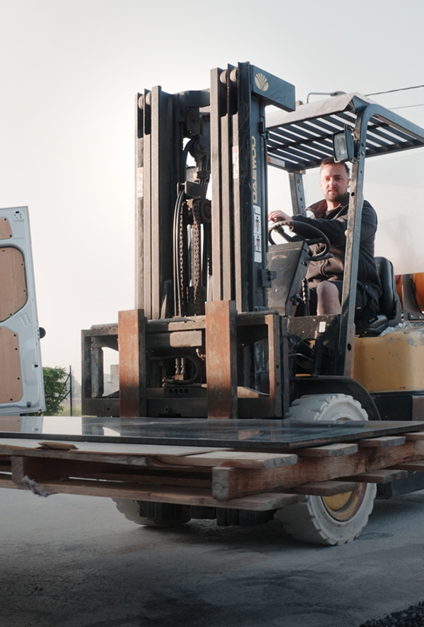 Homme conduisant un chariot élévateur transportant des plaques de métal sur une palette en bois en extérieur.