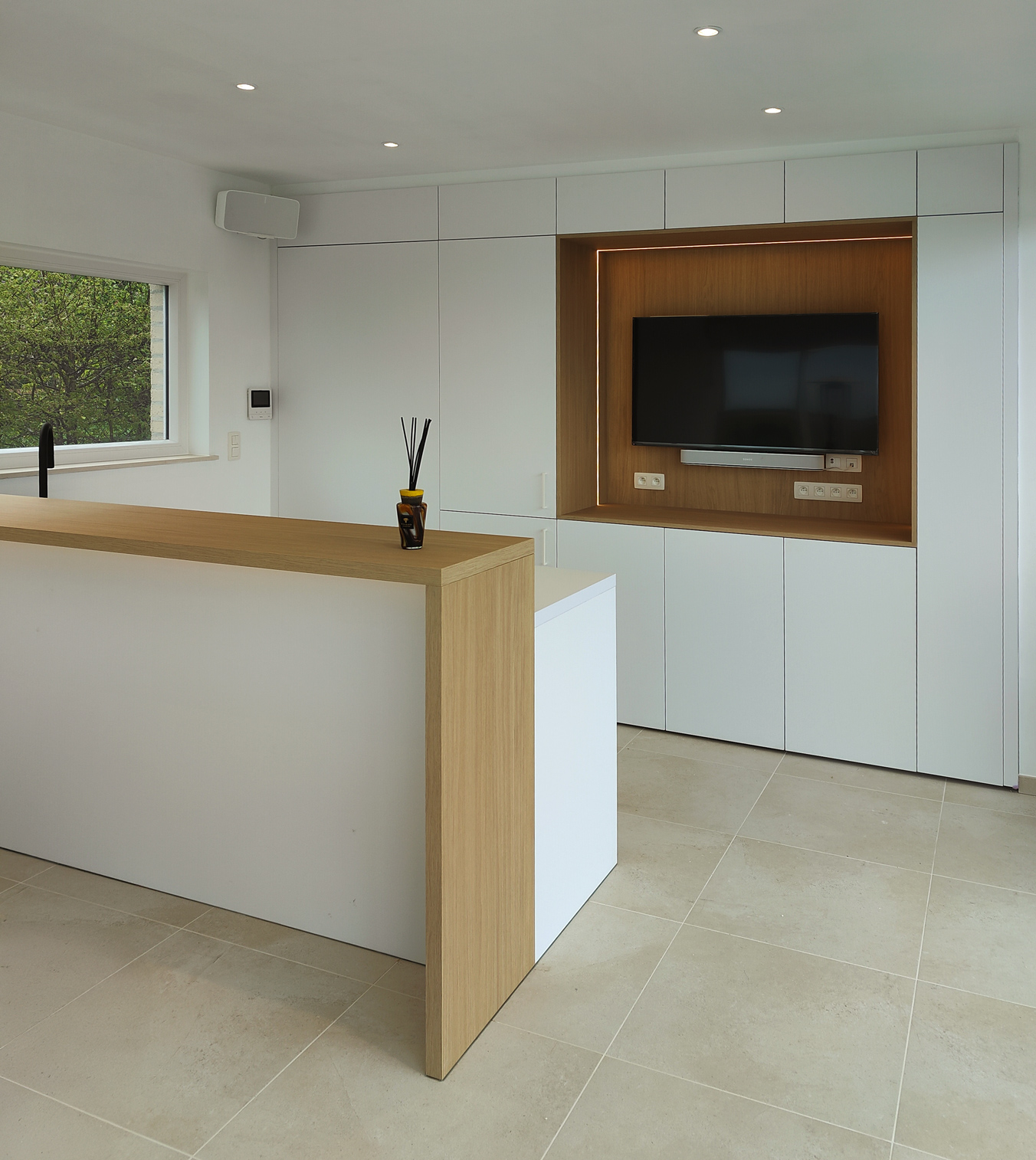 Cuisine moderne avec armoires blanches, un îlot avec un comptoir en bois clair et une télévision encastrée dans un mur en bois.