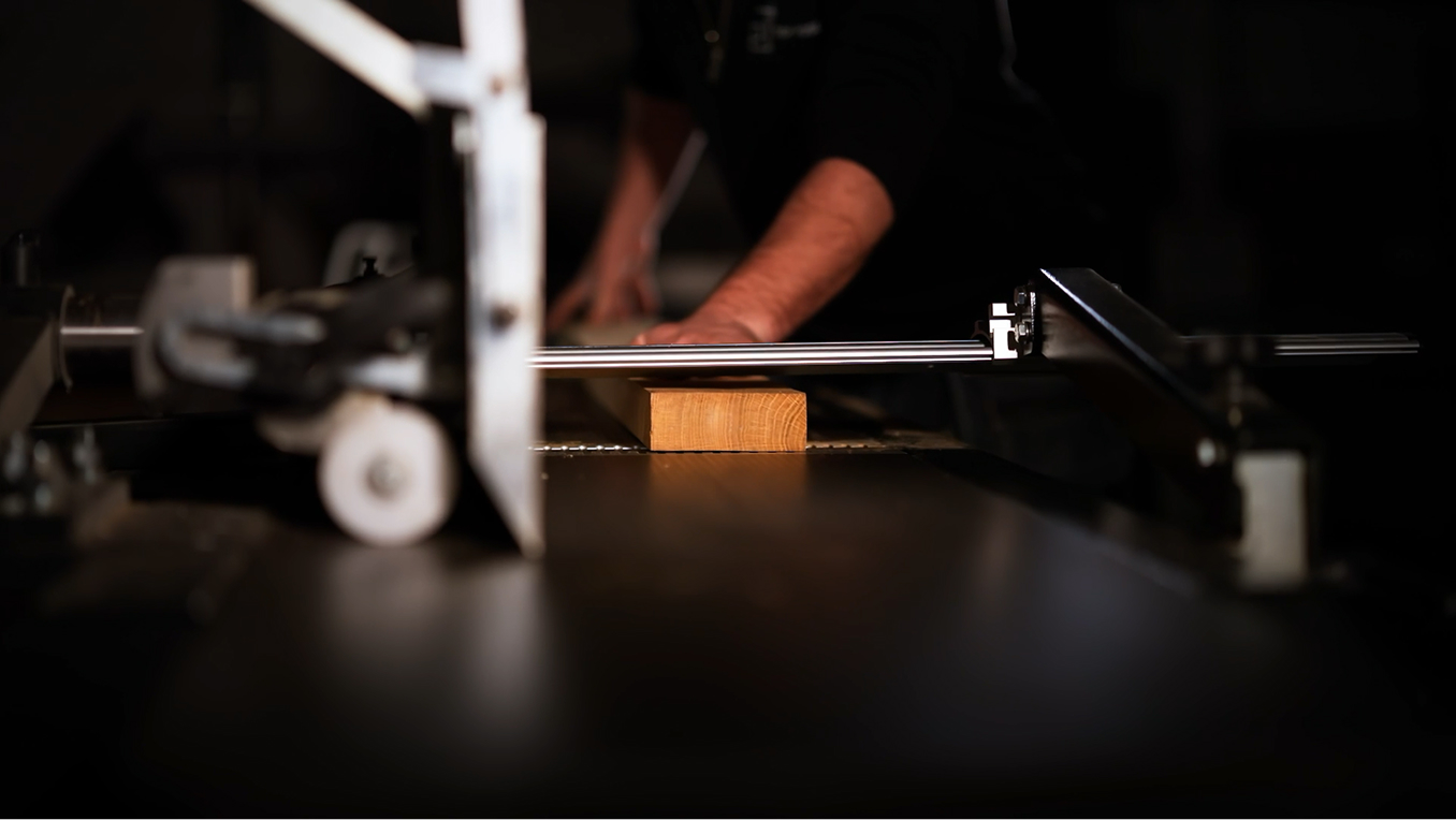 Person insérant une pièce de bois sous une lame de scie dans un atelier sombre.