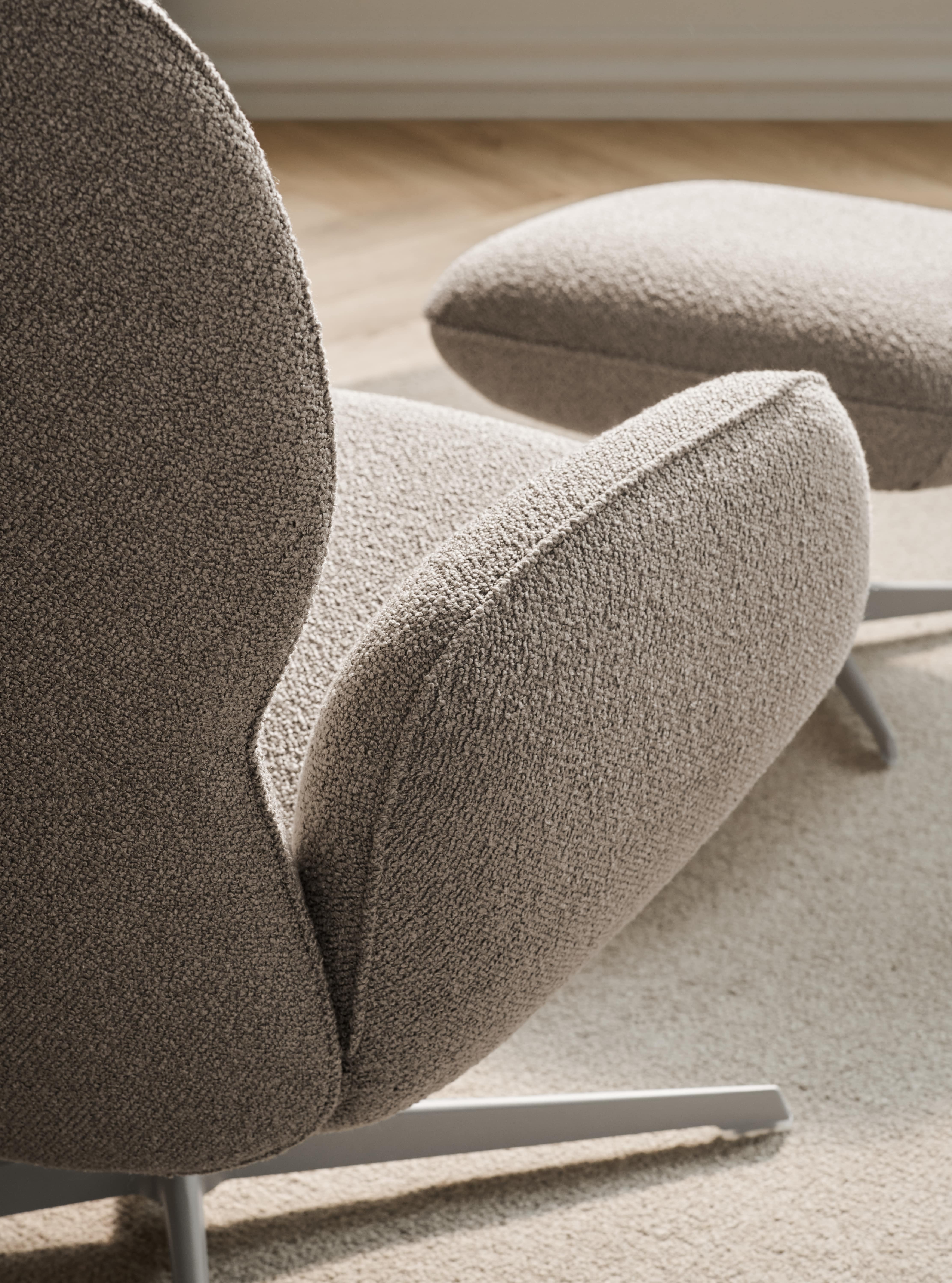 Détail d'un fauteuil et d'un repose-pieds en tissu bouclé beige avec base métallique grise sur un tapis clair.