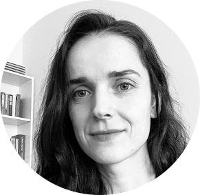 Black and white portrait of a woman with long dark hair and light eyes, smiling slightly, with bookshelves in the background.