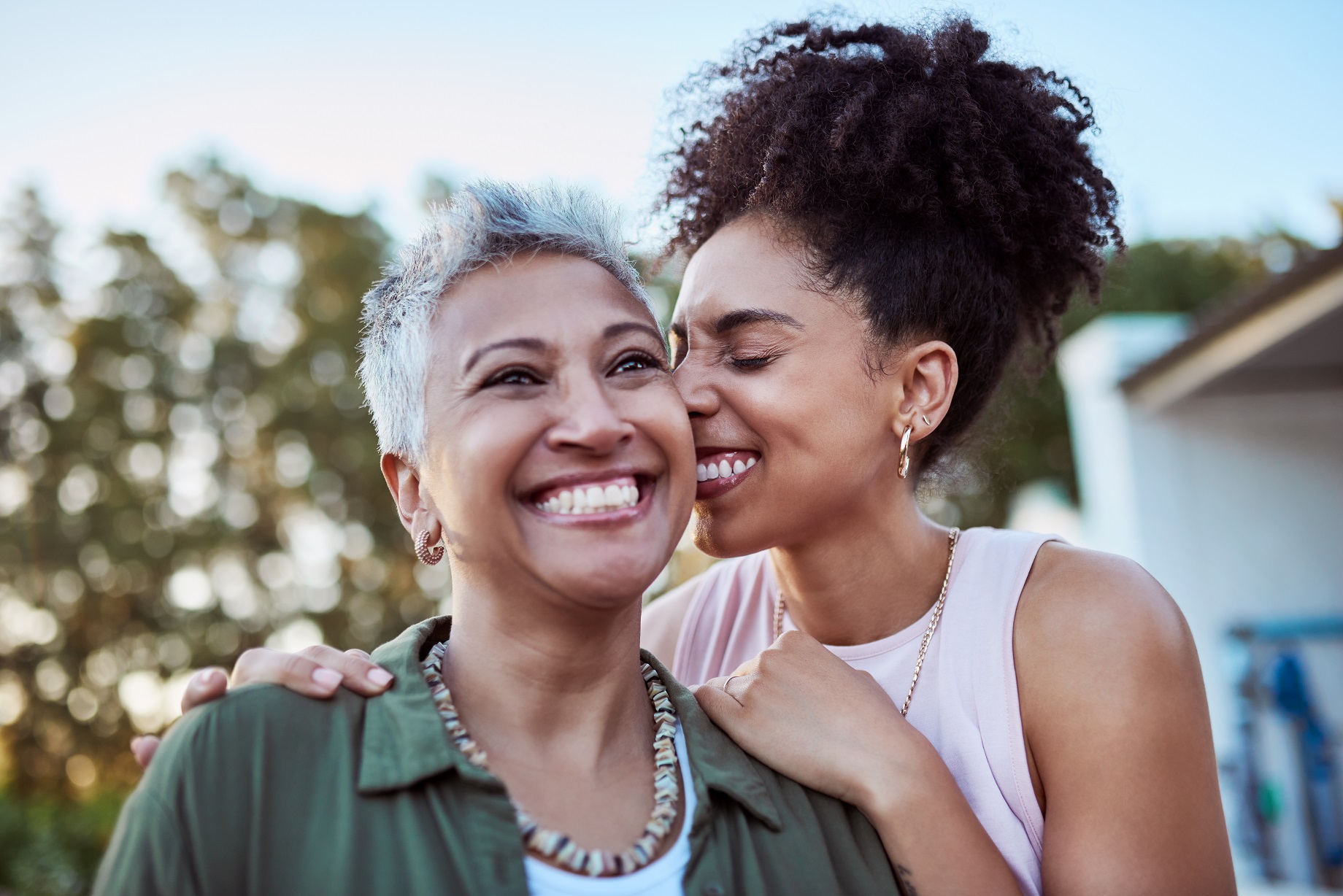 An adult daughter hugging her smiling mother outdoors