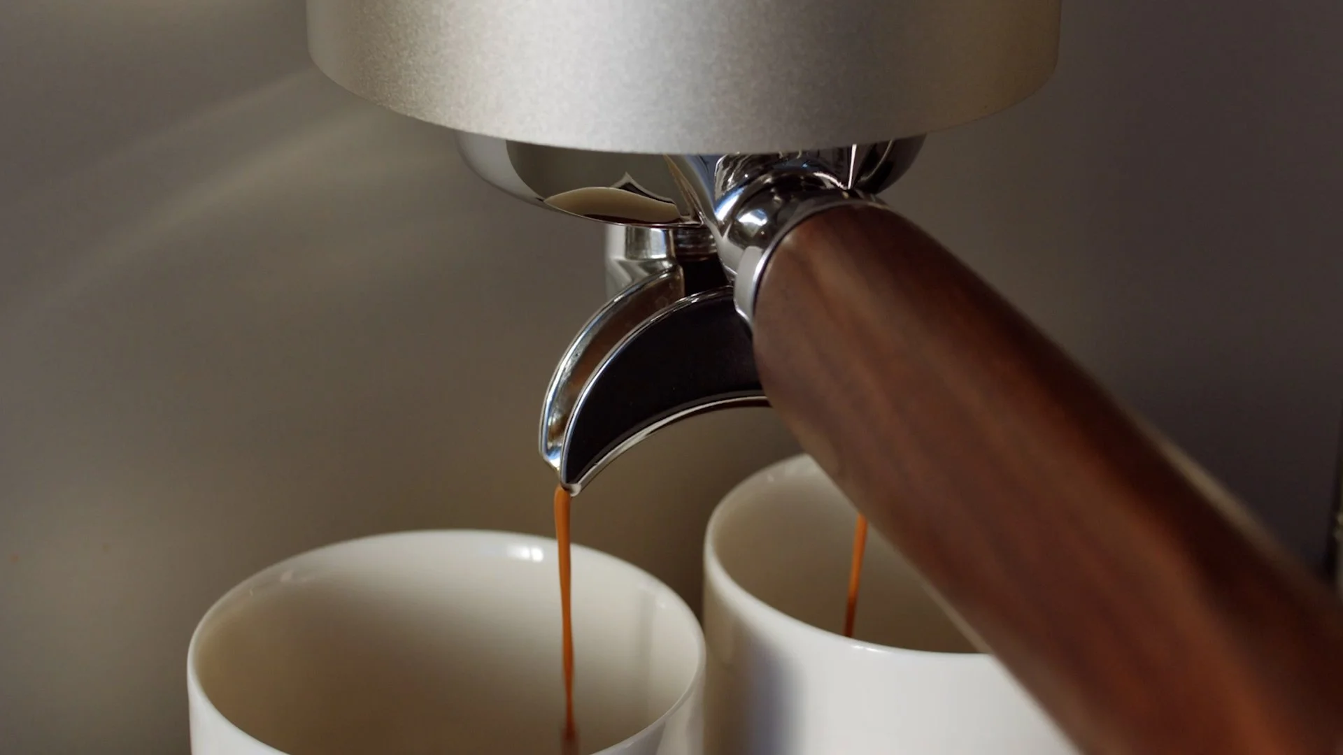 Close-up of espresso machine with wooden handle pouring coffee into two white cups.