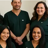 Four smiling healthcare professionals wearing dark green scrubs posing together against a light background.