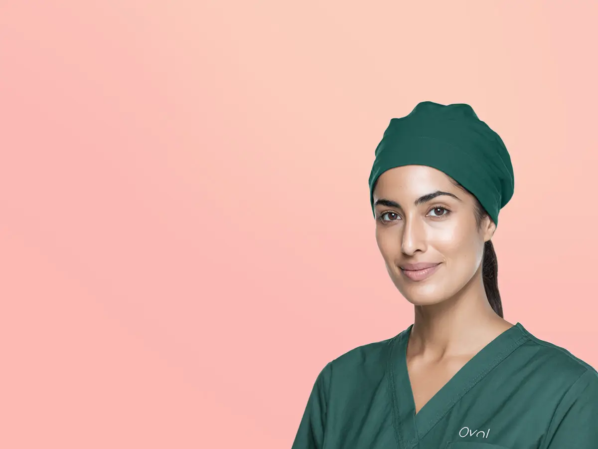 Smiling female medical professional wearing green scrubs and matching surgical cap against a peach background.
