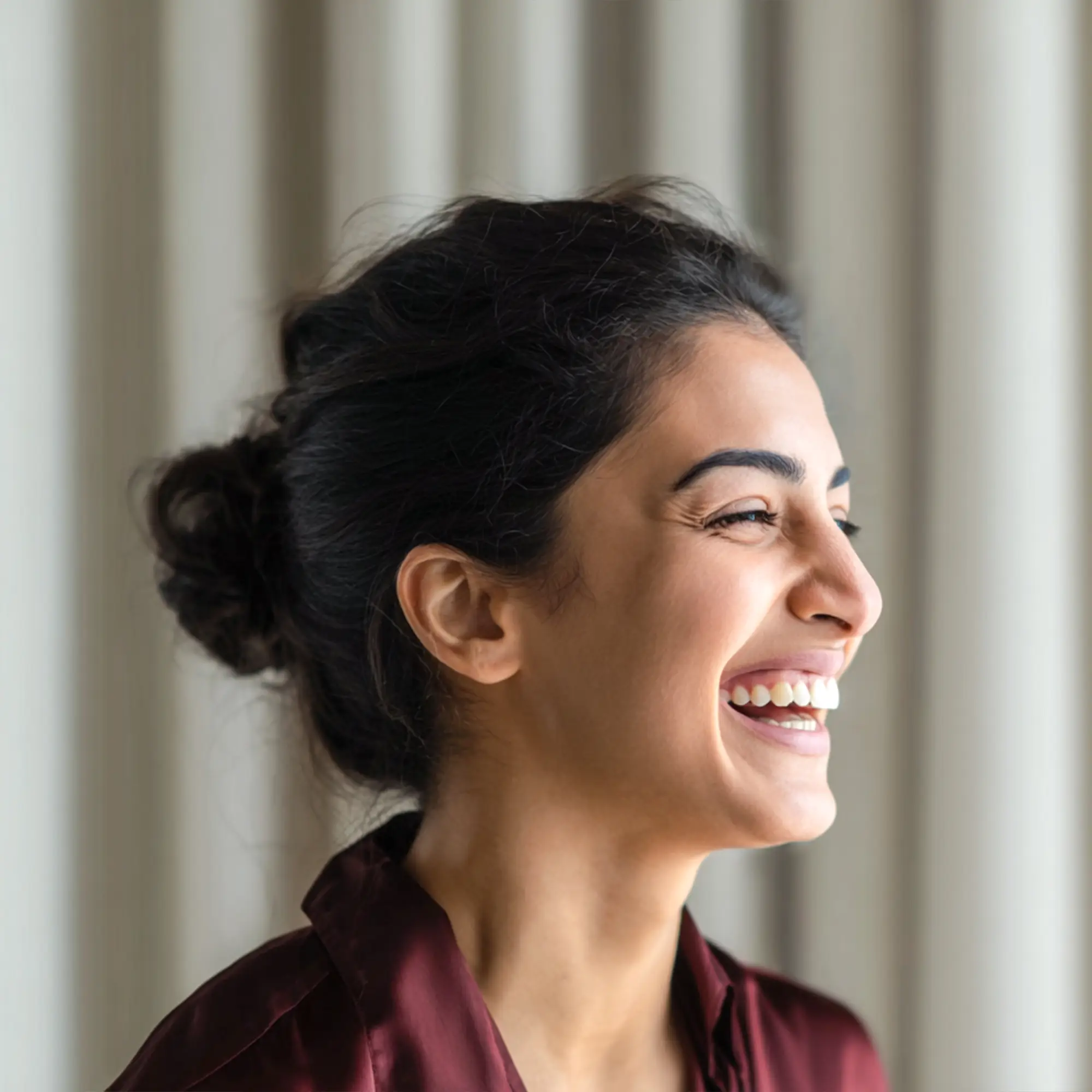 Smiling woman with dark hair tied back, wearing a dark red shirt, looking to the right.