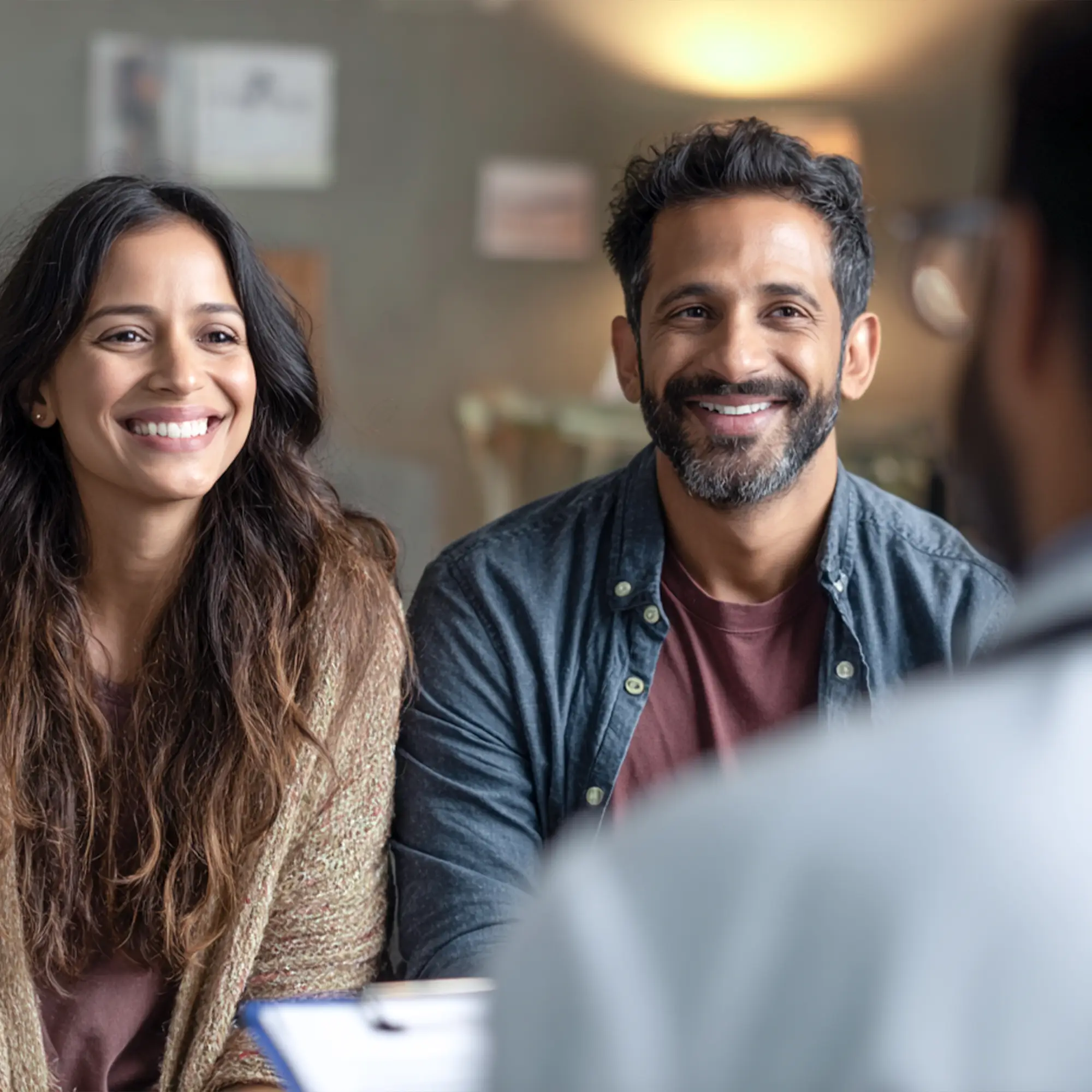 Smiling couple attentively listening to a professional in a cozy indoor setting.