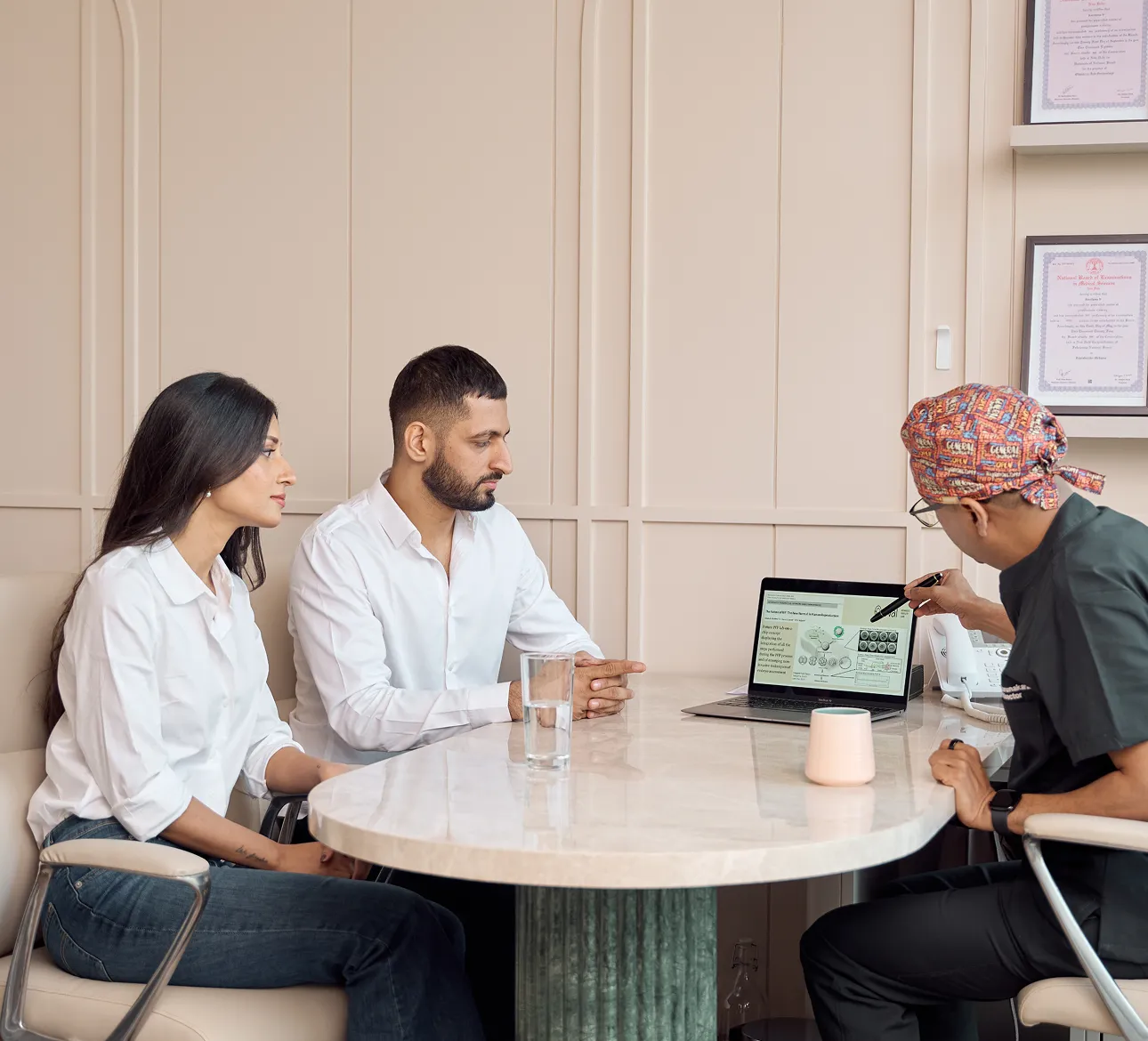 Two patients attentively listening to a doctor explaining medical images on a laptop at a round table.