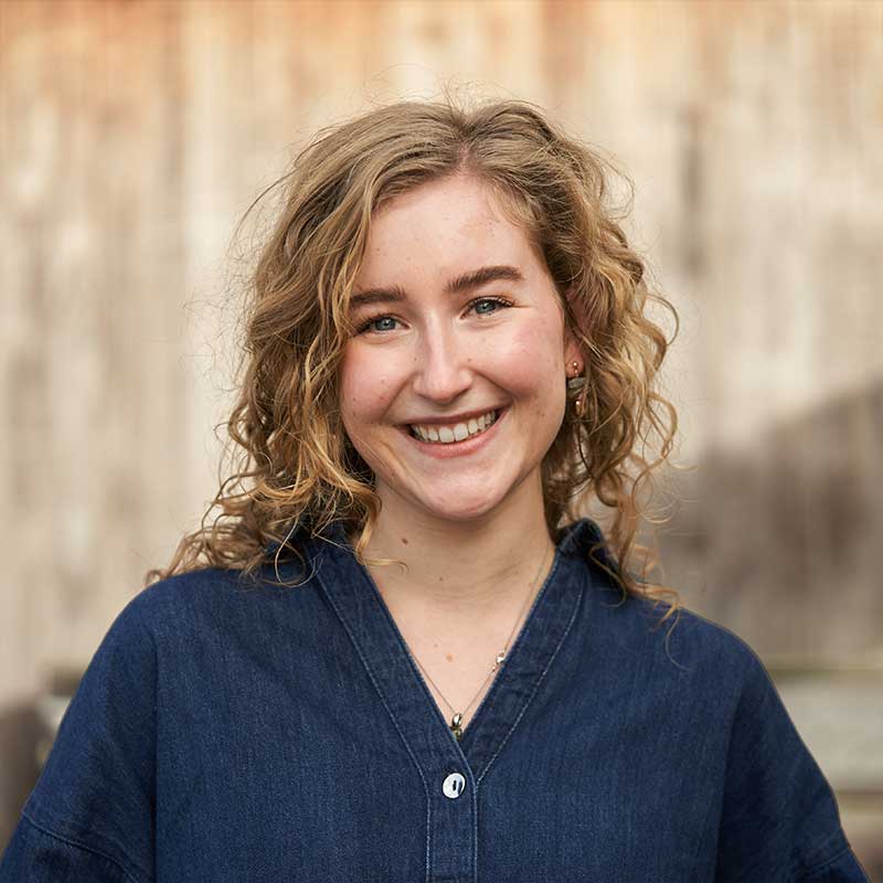 Smiling young woman with blonde hair wearing a blue shirt.