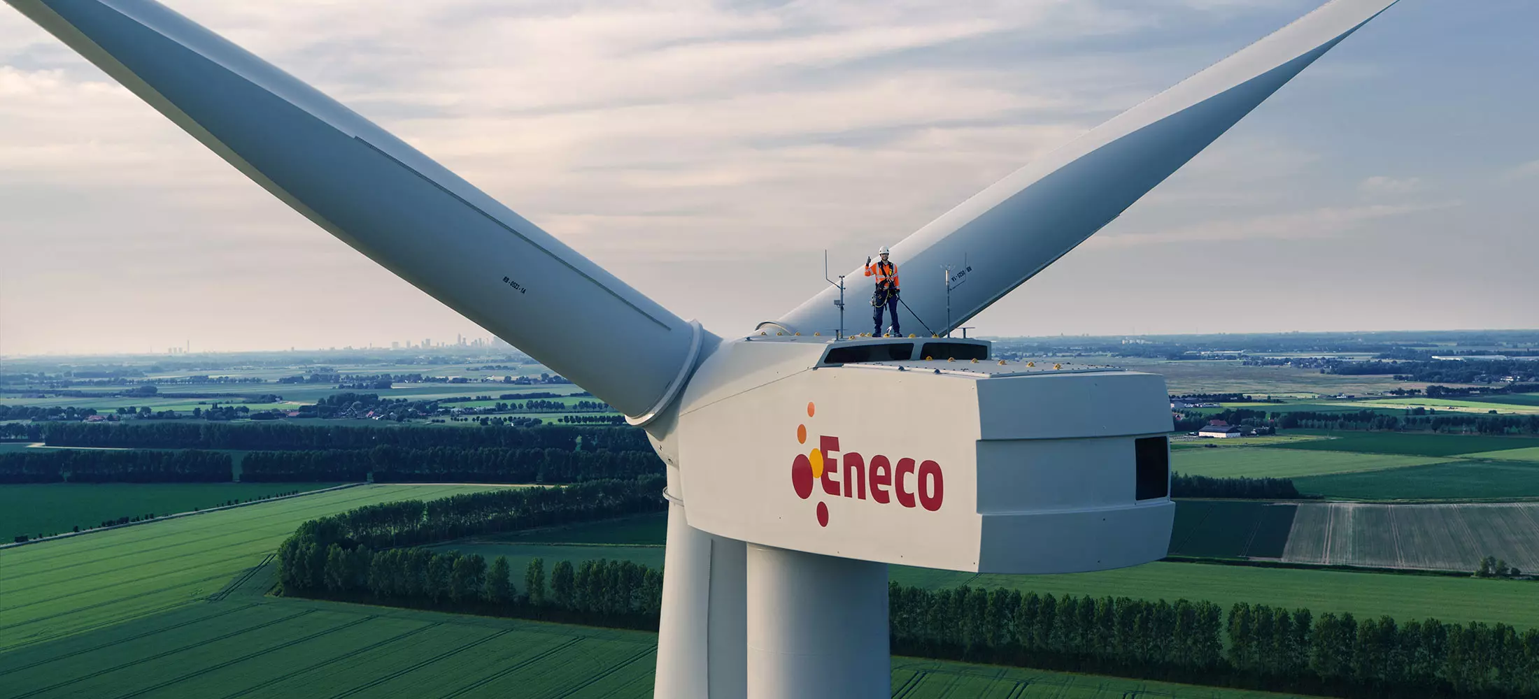 Monteur bovenop een windmolen — symbool voor duurzame energie en samenwerking met Eneco.