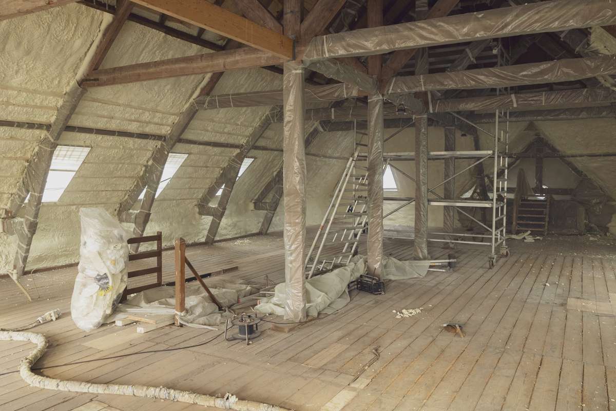 Monteur spuit isolatieschuim aan de binnenkant van een oud dak — vakkundige dakisolatie voor energiezuinige woningen.