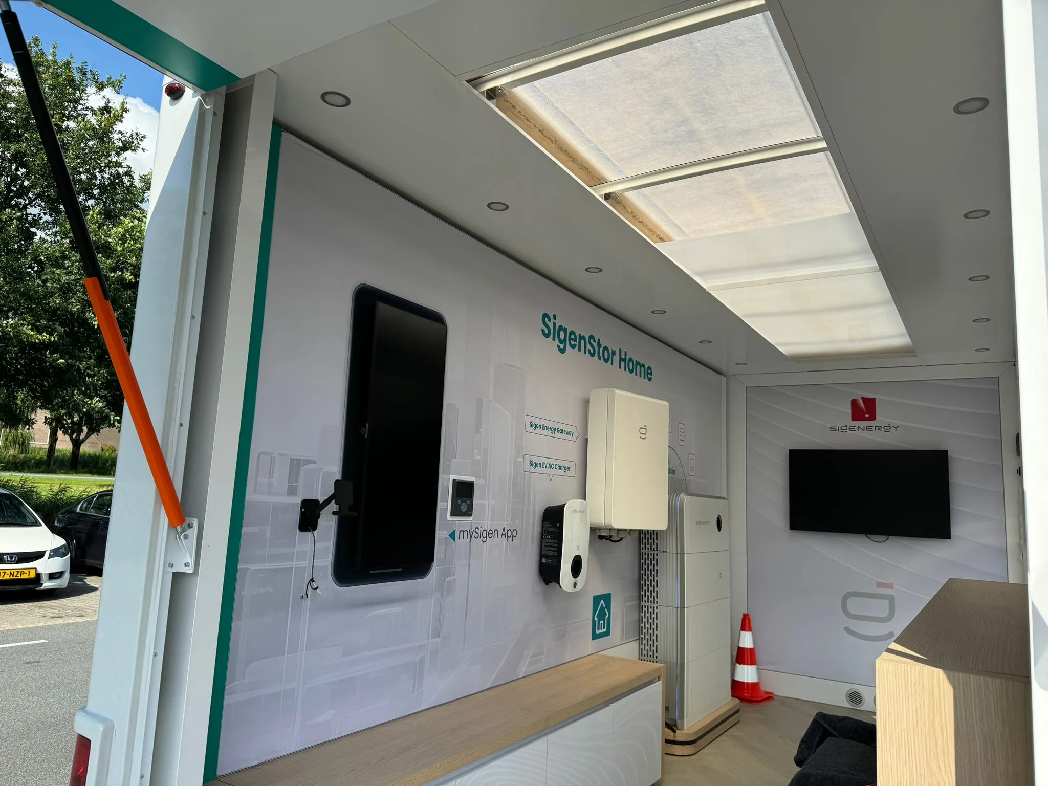 Interieur van een mobiele showroom met SigenStor Home energiemodules en een tv-scherm aan de muur.