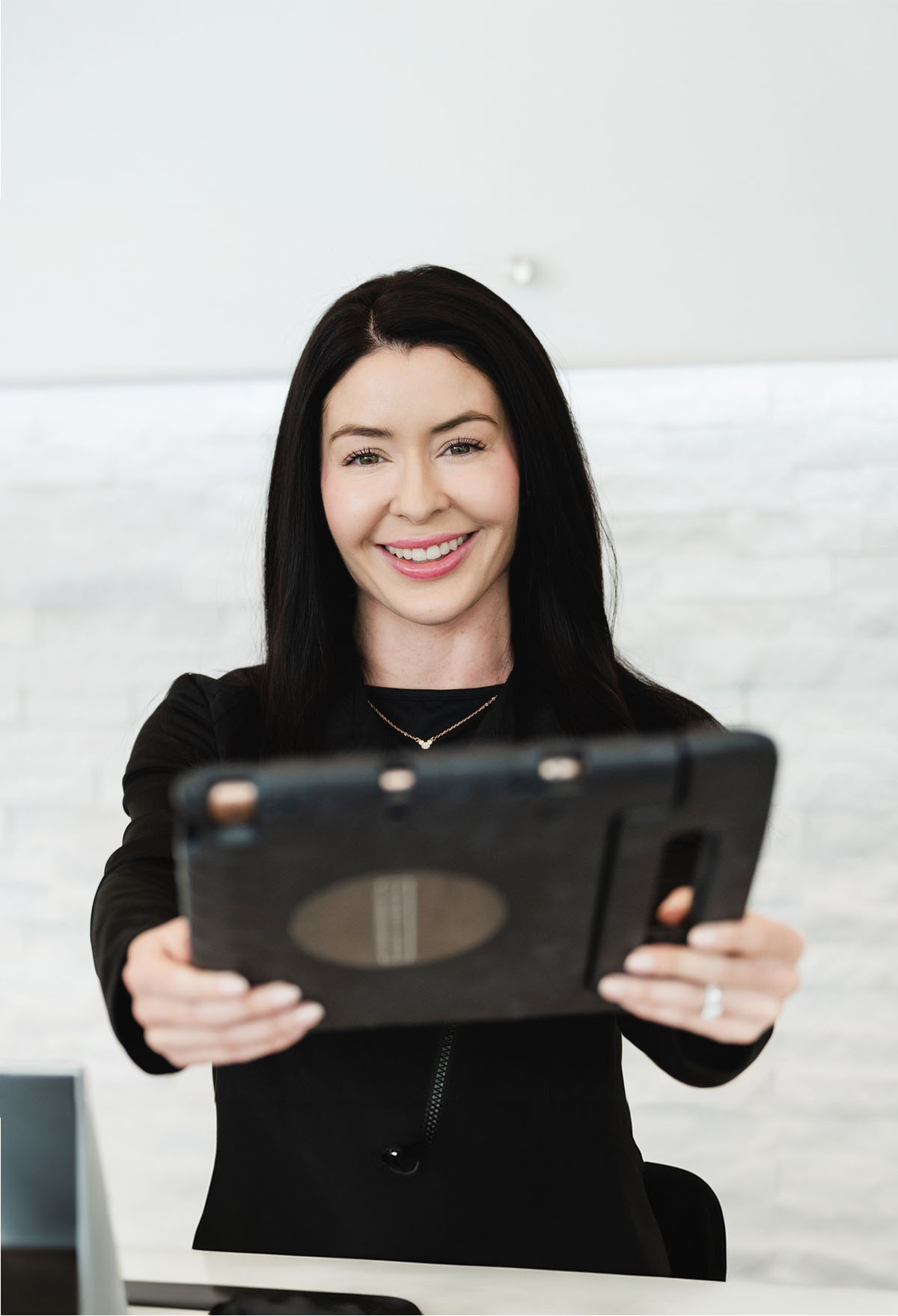 Smiling woman with long black hair holding a tablet towards the camera.