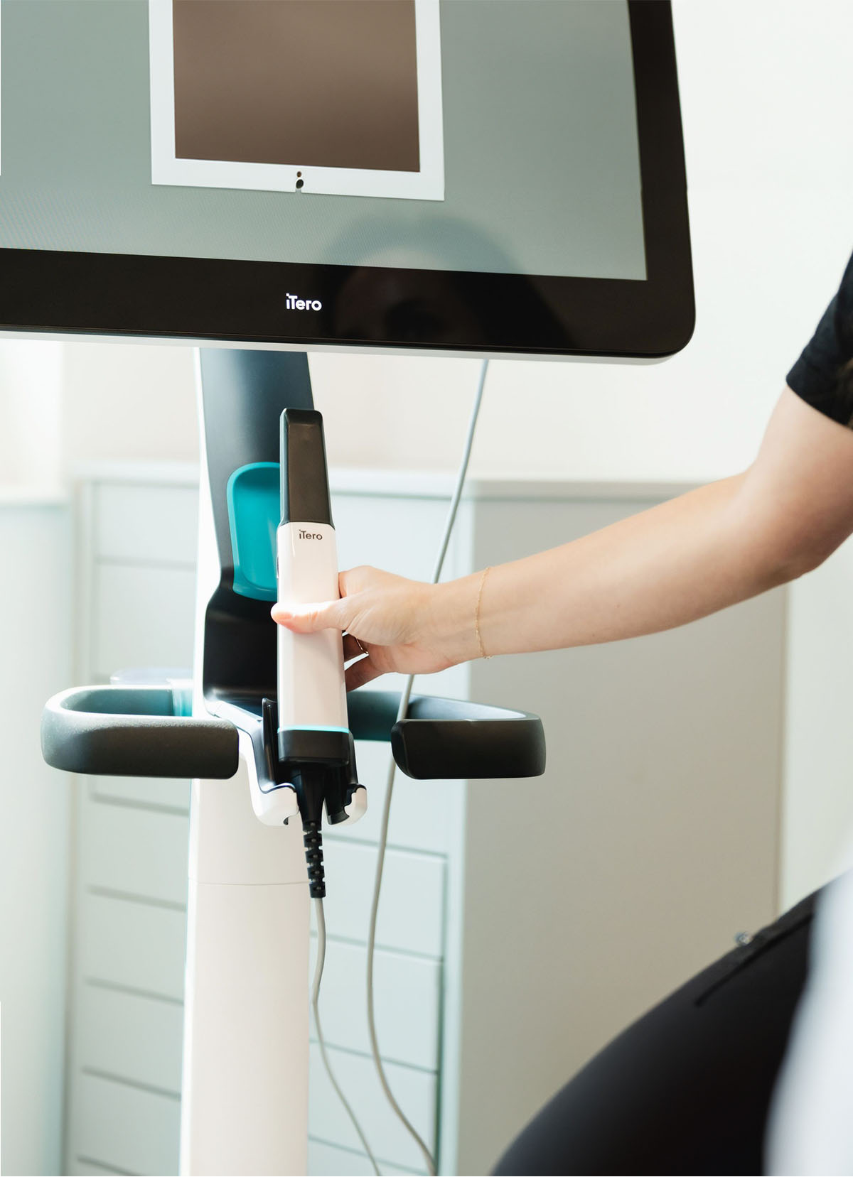 Person holding an iTero dental scanner attached to a monitor in a clinical setting.