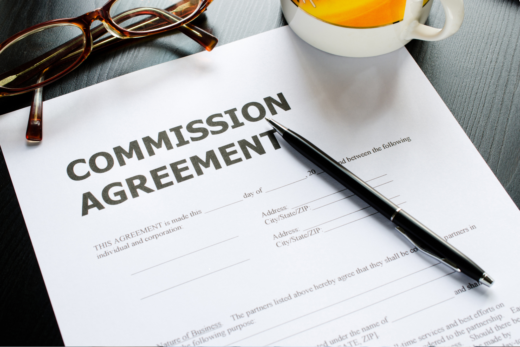 Mehrere Lebensläufe mit einer Brille darauf liegen auf einem Holztisch neben einem Laptop und einer kleinen Uhr.