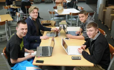 four people sitting at table on laptops smiling