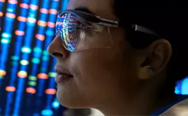 scientist wearing glasses with computer lights in background