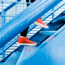 Person wearing bright orange sneakers climbing blue metal stairs.