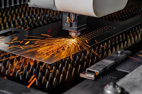 Laser cutting machine engraving sparks onto a metal sheet on a spiked bed.