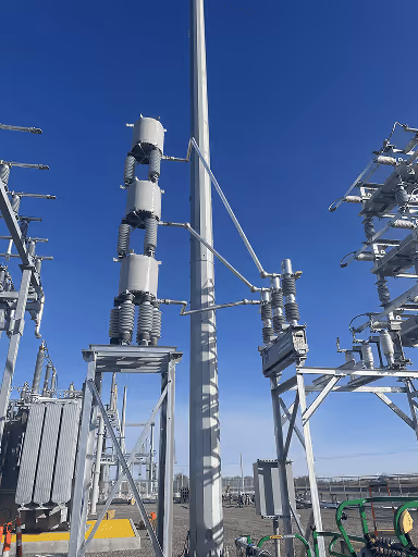 High-voltage electrical substation equipment with insulators and transformers under a clear blue sky.