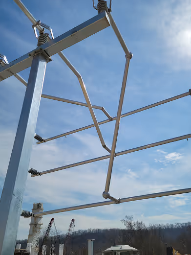 Metal framework structure with insulators against a partly cloudy blue sky and distant construction cranes.