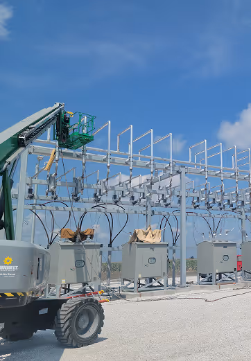 Outdoor electrical substation equipment with a green utility lift under a blue sky.