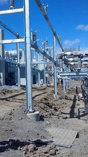 Electrical substation equipment and metal framework installed on muddy ground under a clear blue sky.