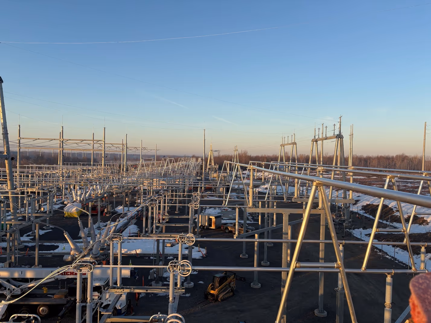 Electrical substation infrastructure with metal frameworks, insulators, and power lines under a clear blue sky at sunset.