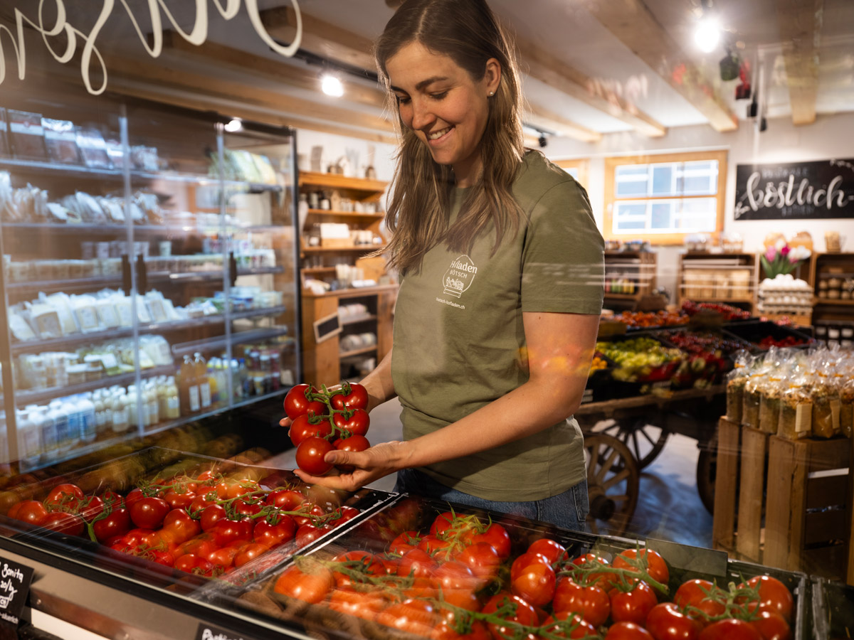 Frau hält Tomaten an ihrem Marktstand in einem hellen, gut sortierten Laden.