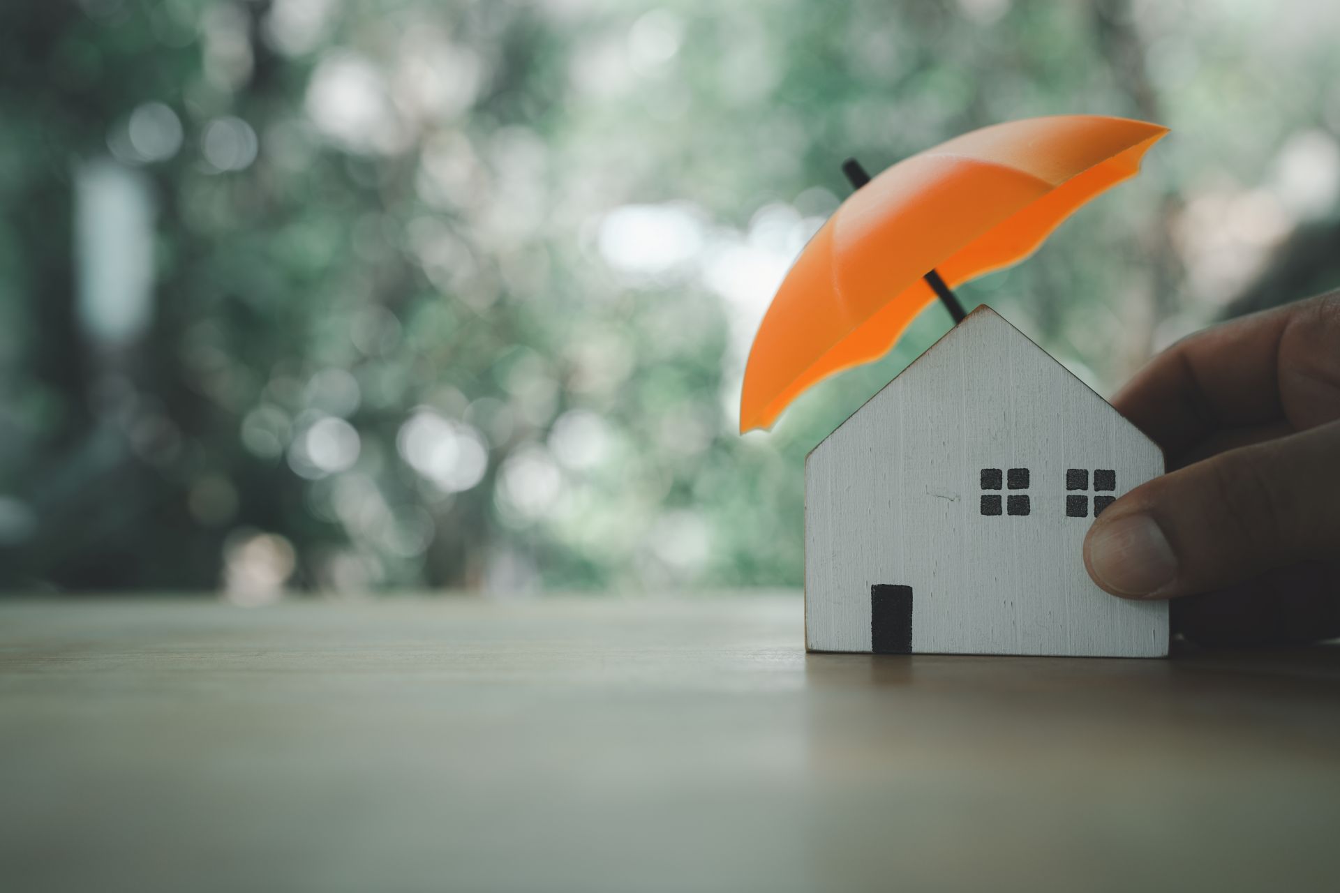 Model toy home with orange umbrella above it to symbolize protection or insured