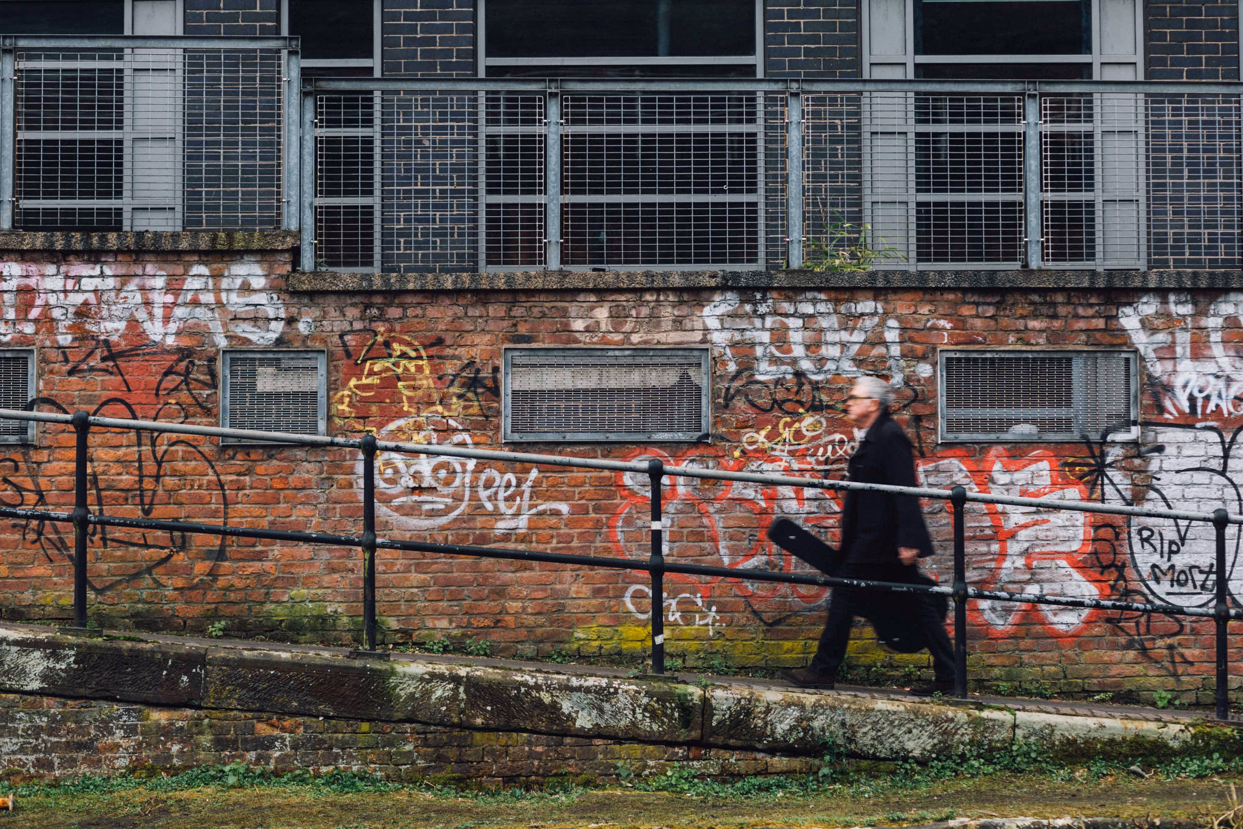 man walks along castlefield canal with a guitar case posing for a promotional photo