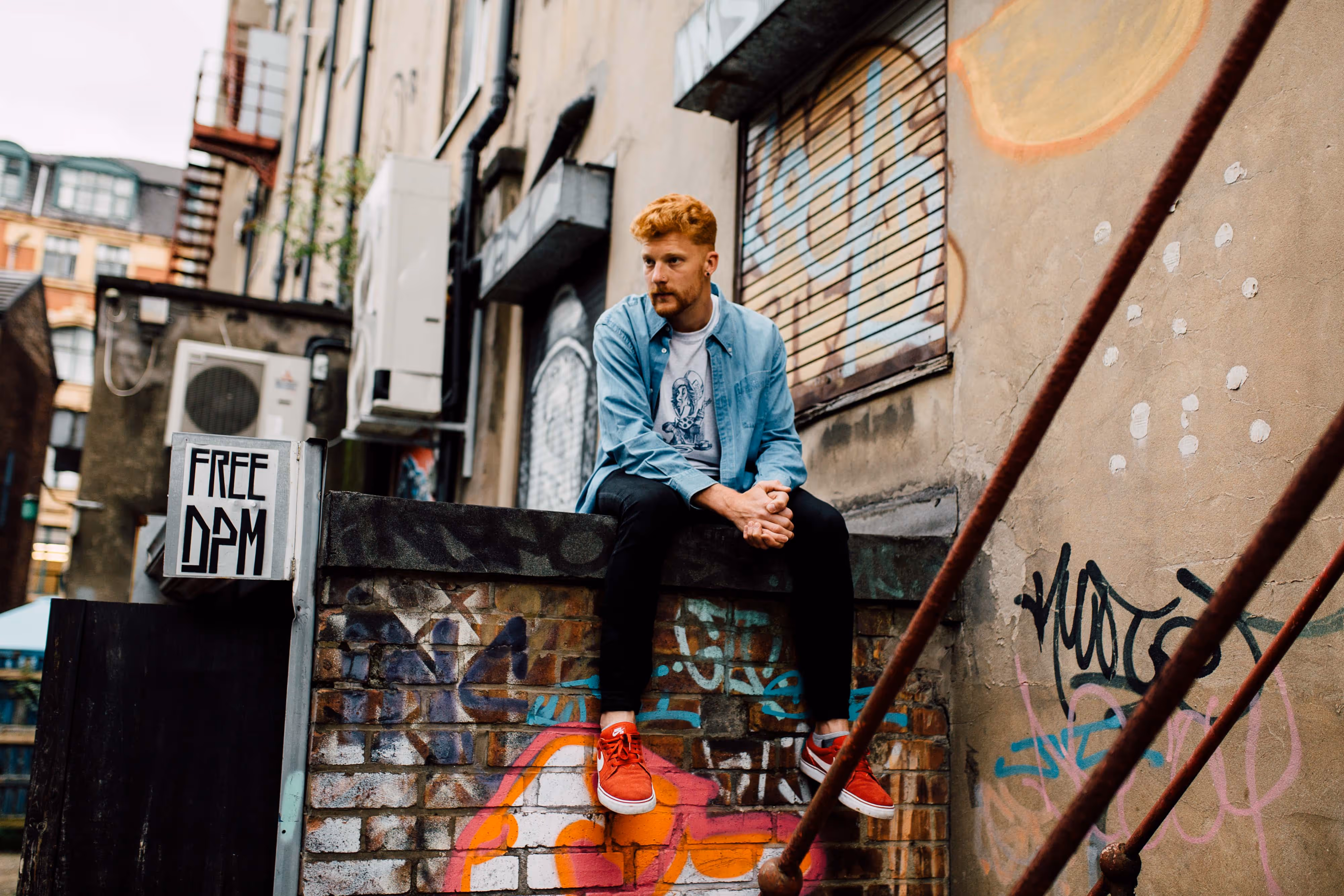natural light press shot of rapper sitting on graffiti wall