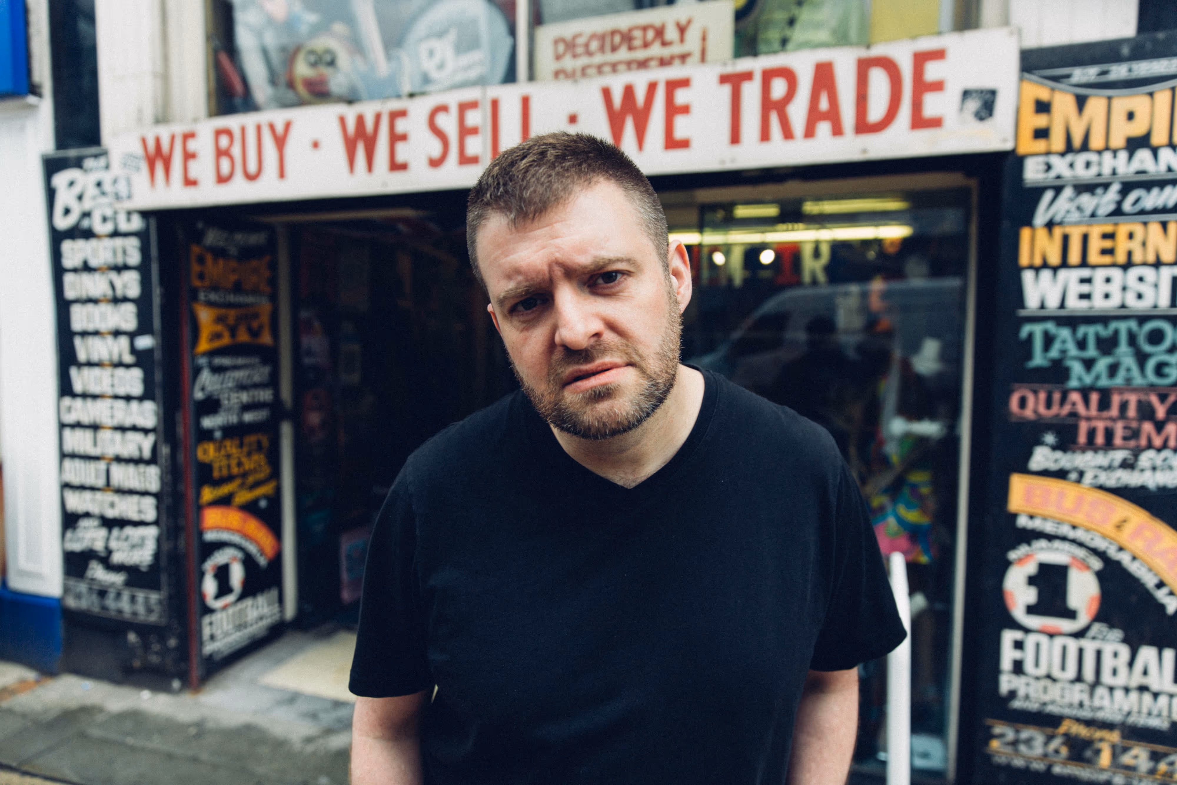 guitarist leans towards the camera in front of a vintage style shop in NQ
