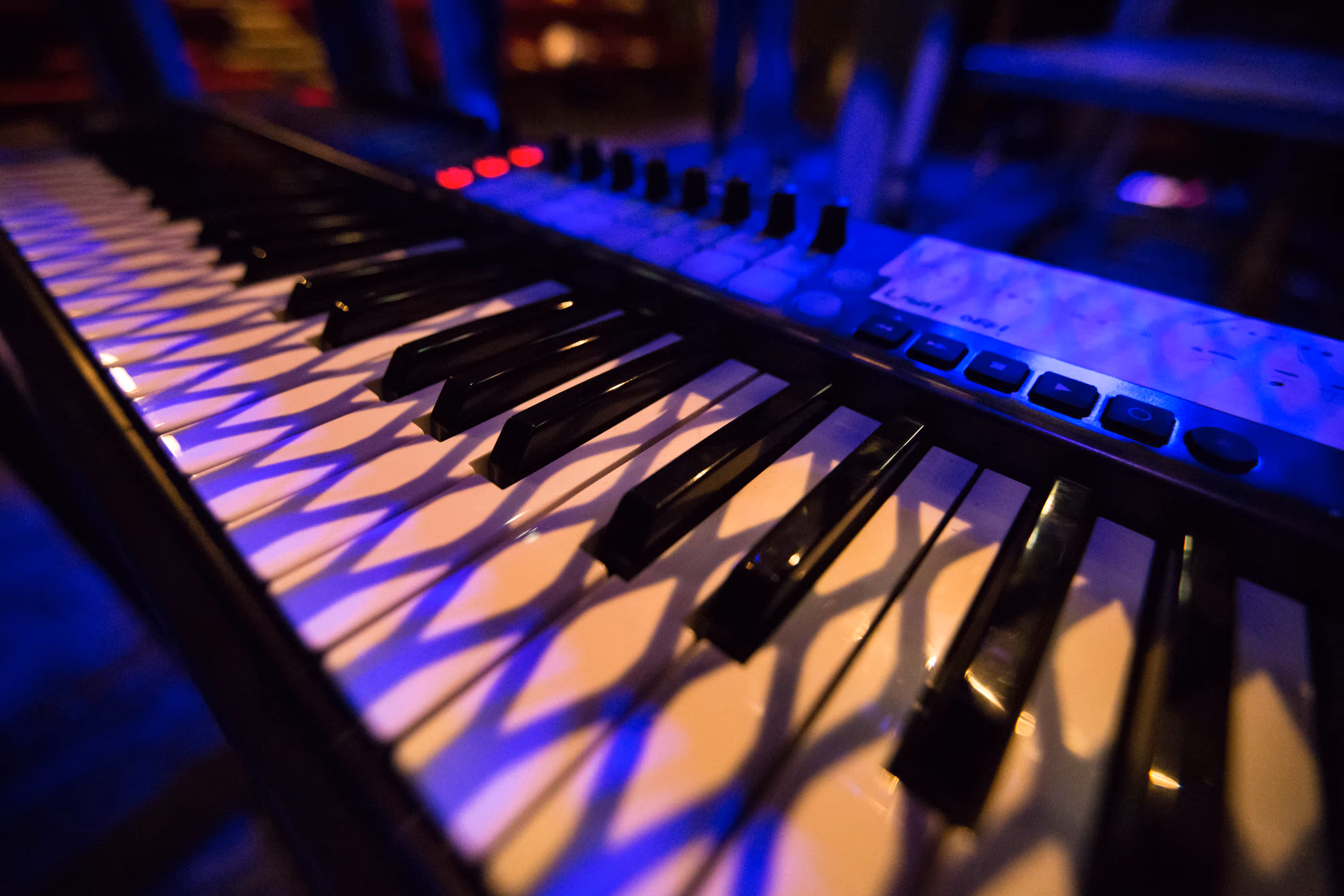 Moody theatre lighting bathes a keyboard in blue and purple hues, dramatic shadows falling across the glossy keys in close-up.