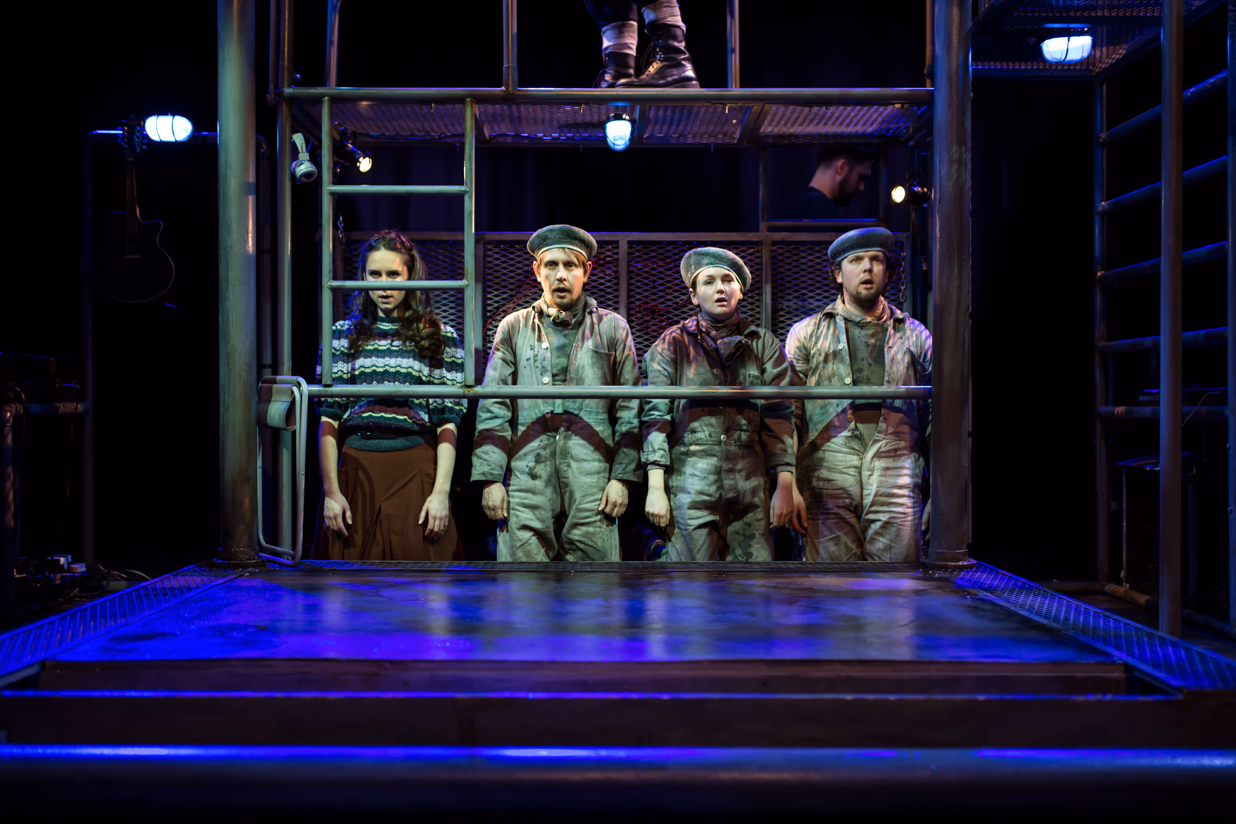 A cast of performers stands together on stage, illuminated by theatre lights as I capture the energy of their live performance.