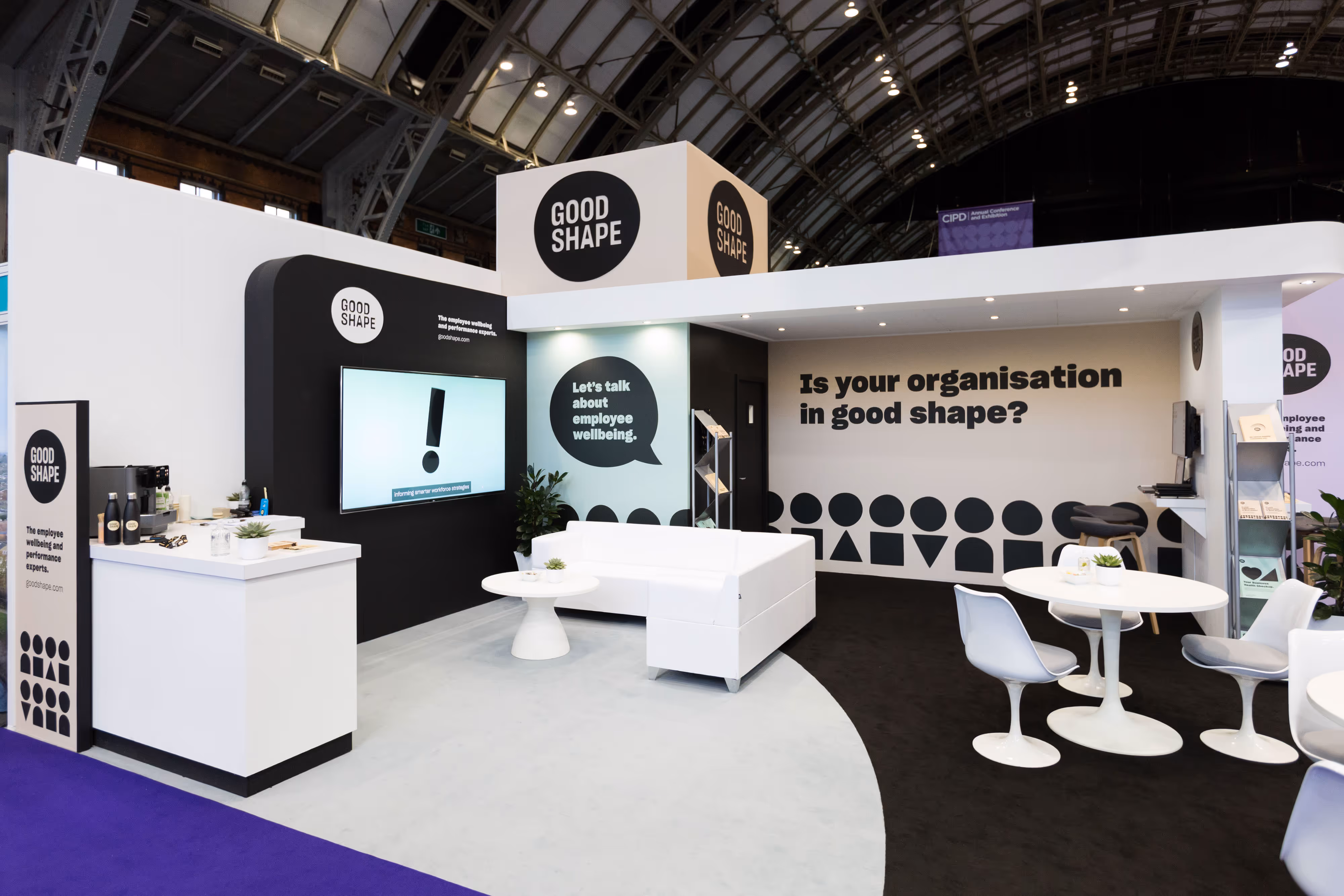 Exhibition stand for with modern furniture and wellness messaging inside Manchester Central, a large convention centre.