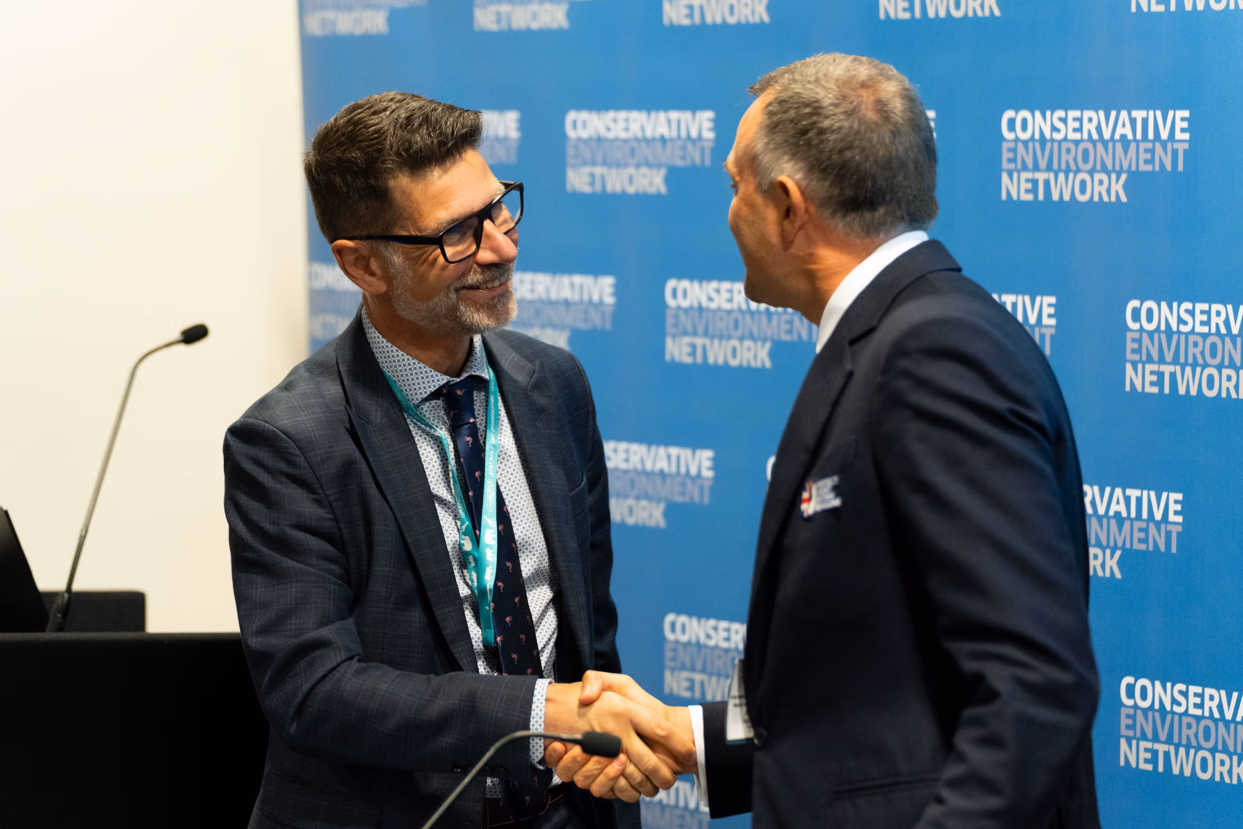 Men in suits smiling and shaking hands at a Conservative Environment Network fringe event at a political party conference.