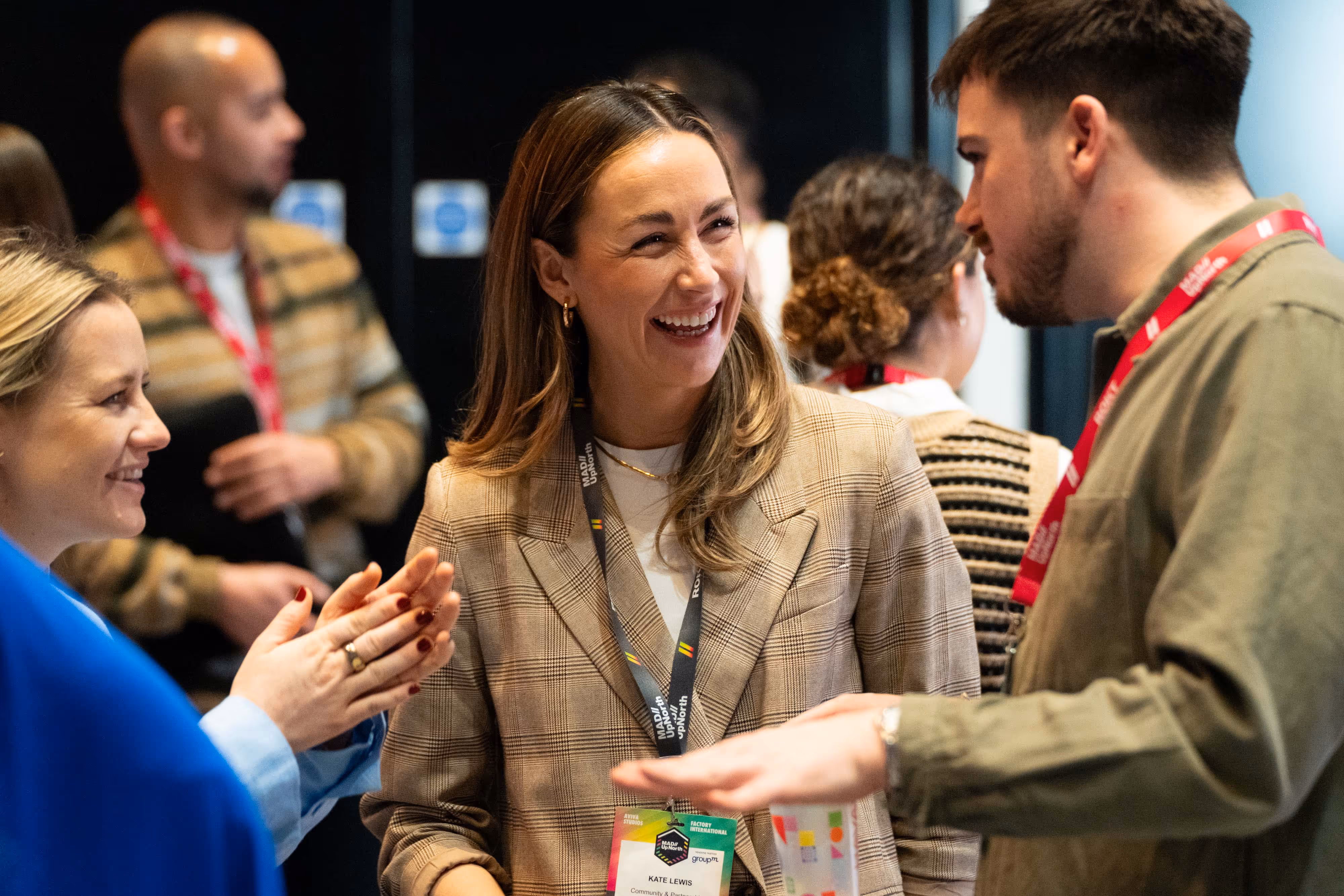 Three people in conversation at a professional event, wearing name badges and smiling warmly.
