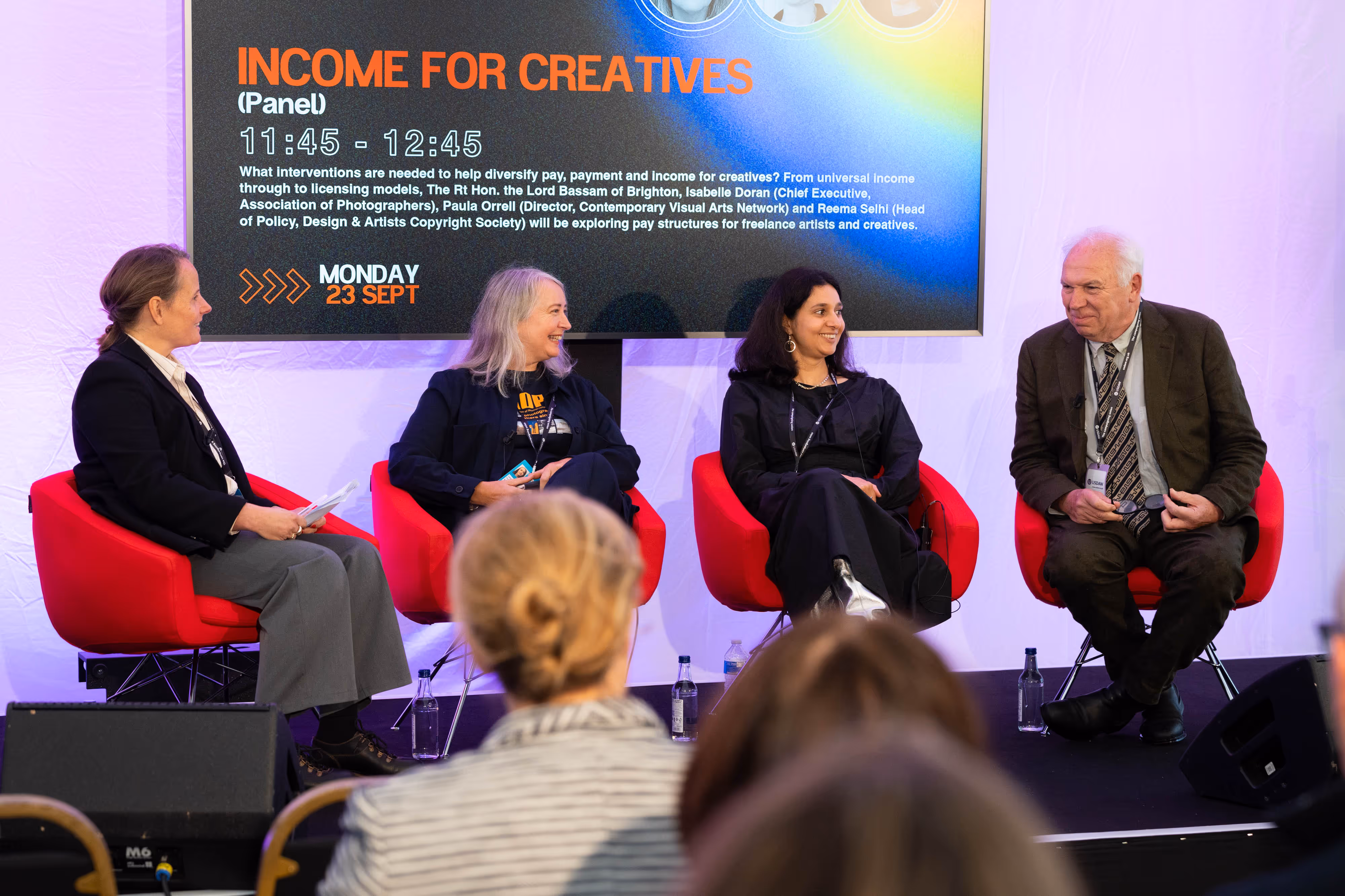 Four panellists sit on stage discussing "Income for Creatives" at an event, with an audience watching in the foreground.