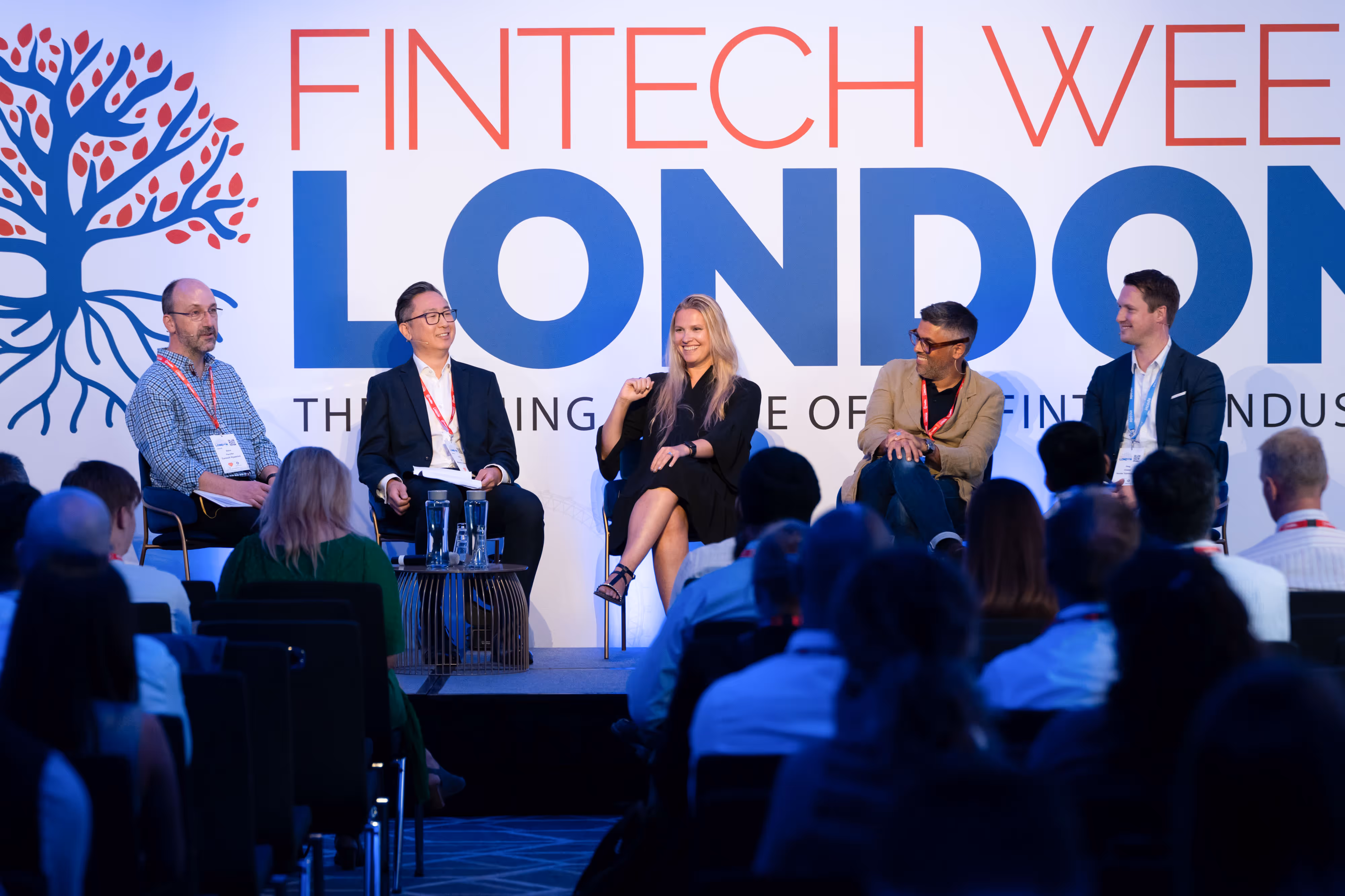 Five panellists sit on stage speaking at the Fintech Week London event, facing an audience in a conference room.