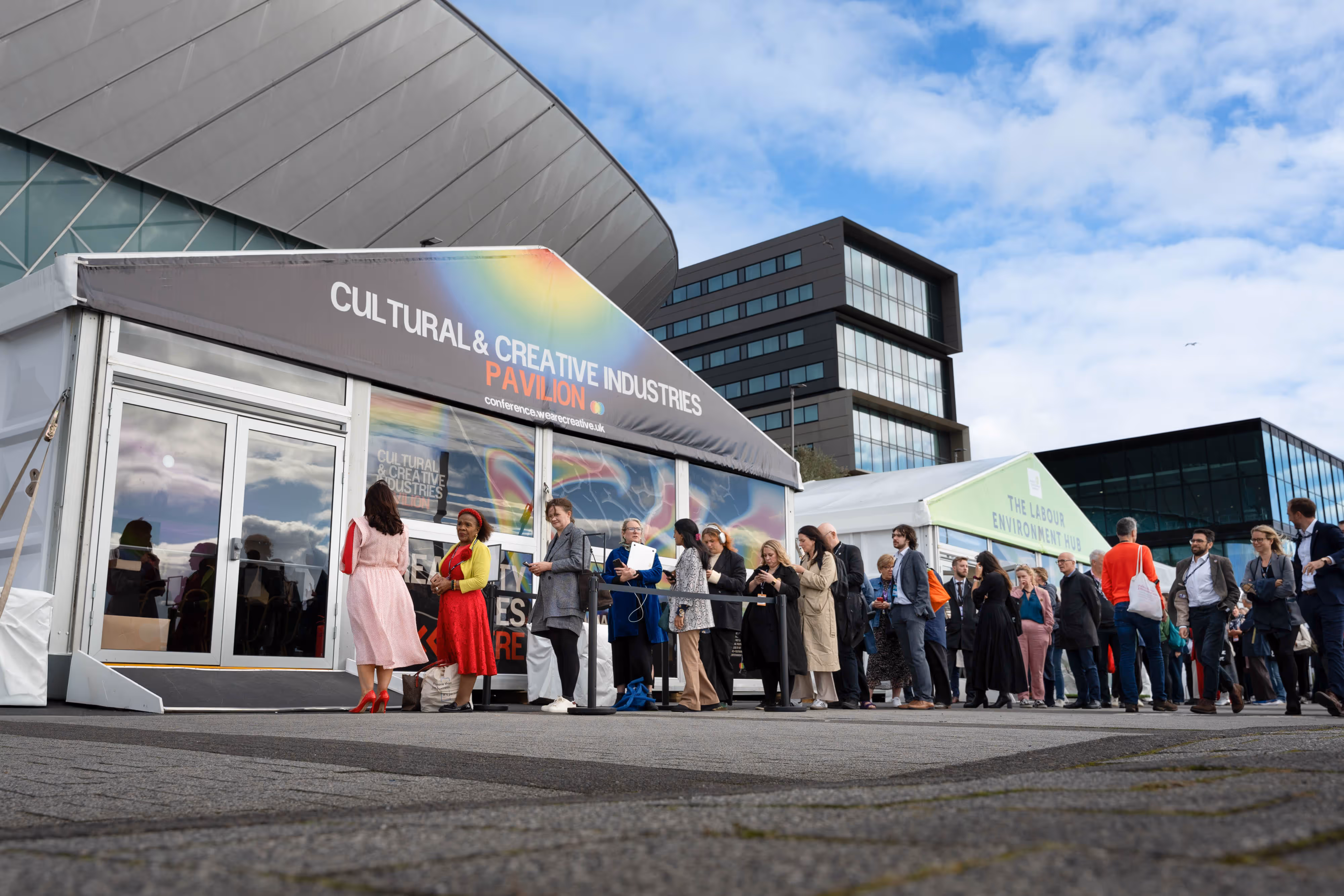 People wait in queue outside a large marquee labelled "Cultural & Creative Industries Pavilion" at a Labour Party Conference.